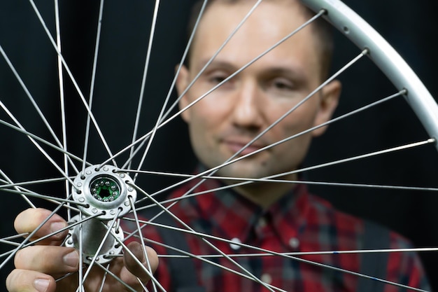 Reparación de bicicletas Un mecánico sostiene en su mano la rueda delantera de una bicicleta de carretera Mantenimiento del buje Reemplazo de grasa y cojinetes Cara del mecánico en el marco