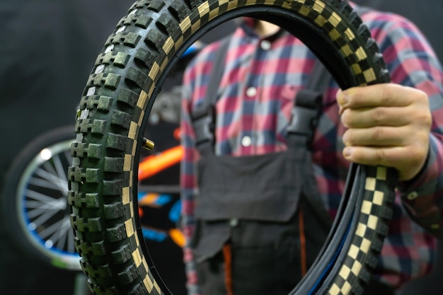 Reparación de bicicletas para niños Un mecánico en el taller sostiene en su mano un viejo neumático desgastado de una bicicleta para niños Mantenimiento de equipos de seguridad de ciclismo para niños