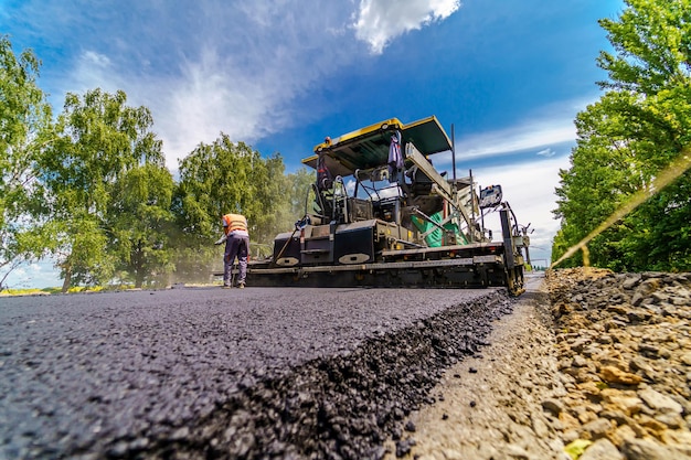 Reparación de carreteras, compactador coloca asfalto. Máquinas especiales pesadas. Extendedora de asfalto en funcionamiento. Vista desde abajo. De cerca.