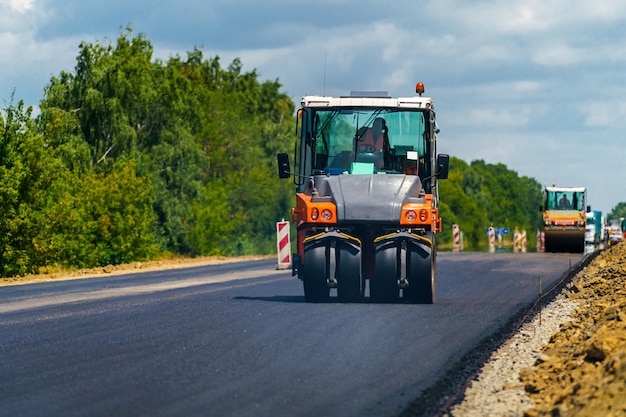 Reparación de carreteras, compactador coloca asfalto. Máquinas especiales pesadas. Extendedora de asfalto en funcionamiento. Vista lateral. De cerca.