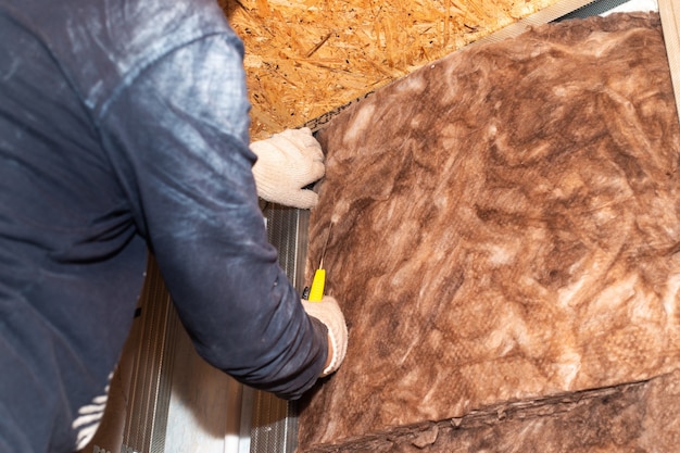 Reparación de la casa. El trabajador aísla las paredes con lana mineral para un posterior revestimiento con placas de yeso. Aislamiento térmico y acústico de viviendas.