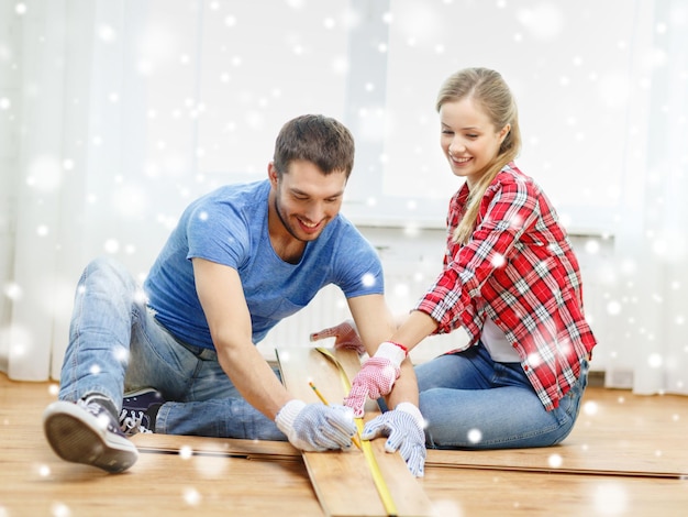 reparación, construcción, familia, personas y concepto de hogar - pareja sonriente midiendo tablones de parquet en el suelo