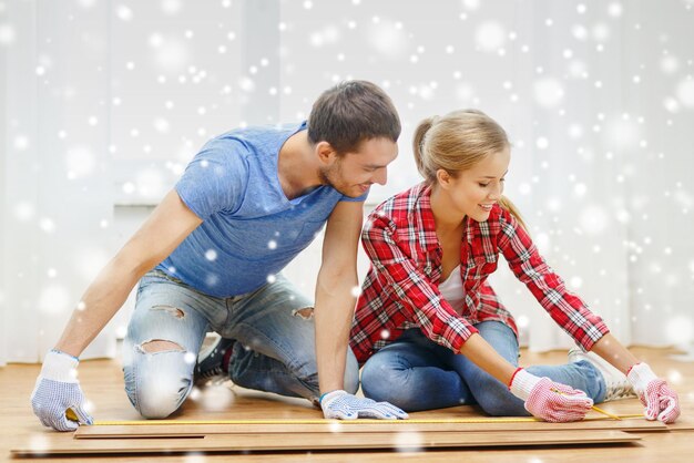 reparación, construcción, familia, personas y concepto de hogar - pareja sonriente midiendo tablones de parquet en el suelo