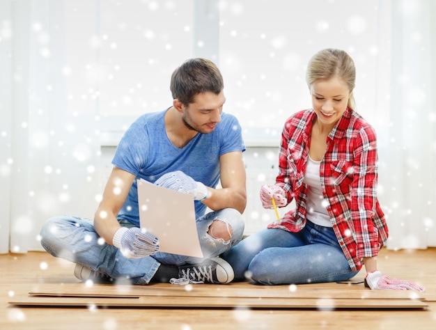 reparación, construcción, familia, personas y concepto de hogar - pareja sonriente midiendo tablones de parquet en el suelo