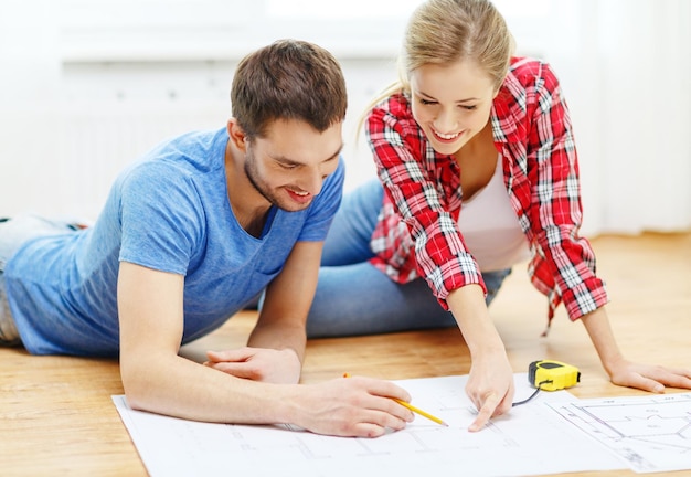 Foto reparación, construcción, renovación y concepto de hogar - pareja sonriente mirando planos en casa