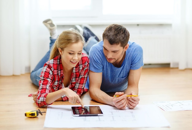 Foto reparación, construcción, renovación y concepto de hogar - pareja sonriente mirando tablet pc en casa