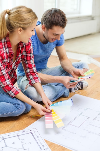 Foto reparación, diseño de interiores, construcción, renovación y concepto de hogar - pareja sonriente mirando muestras de color en casa