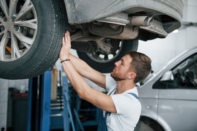 Reparación exitosa. Empleado en el uniforme de color azul trabaja en el salón del automóvil