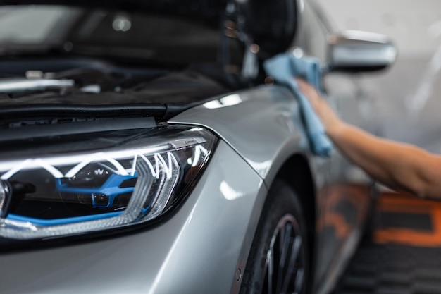 Reparación y lavado de automóviles en la estación de servicio Estudio de detalles Lámparas delanteras ópticas láser Hombre limpia un automóvil con un paño