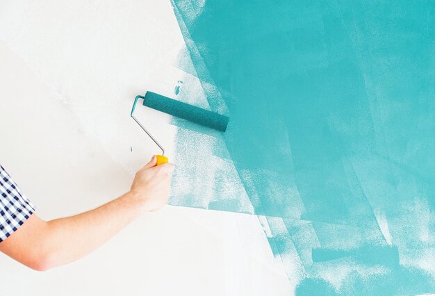 Reparación y mejora del hogar hombre coloreando la pared azul con un rodillo