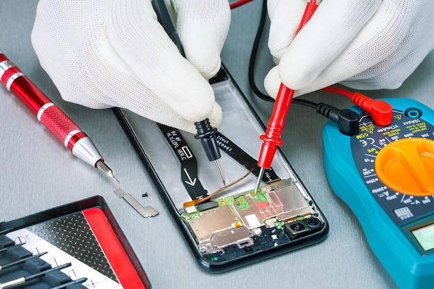 Reparación de smartphone con multímetro en laboratorio. Comprobación de teléfono móvil dañado con multímetro digital.