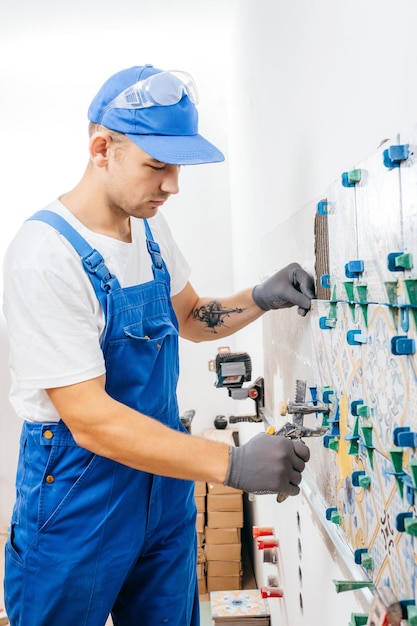 Reparador adulto em um uniforme especial que coloca ladrilhos com sistema de nivelamento de ladrilhos na parede da cozinha em um