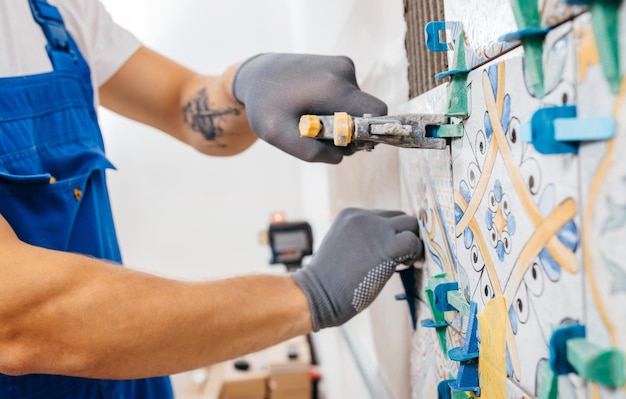 Reparador adulto en un uniforme especial que pone azulejos con sistema de nivelación de azulejos en la pared de la cocina en un