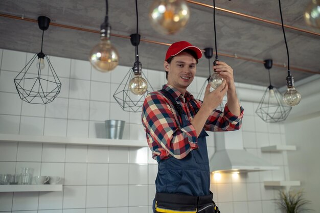 Foto reparador alegre que cambia la bombilla eléctrica en la lámpara pendiente