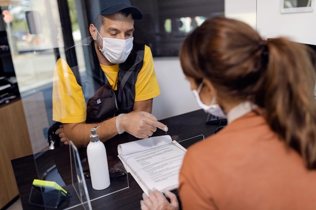 El reparador de automóviles le da al cliente un documento para que lo firme a través del protector contra estornudos en la oficina