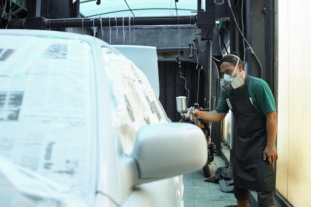 Foto reparador de automóviles en el respirador pintando la carrocería del coche en la cámara de pintura