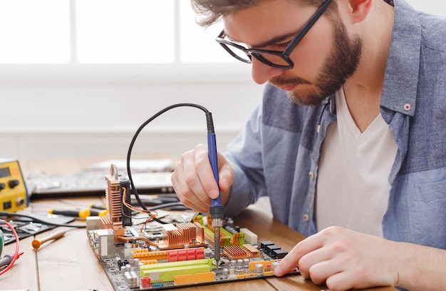 Reparador de circuito de computadora de soldadura en el taller. Joven ingeniero arreglando el componente electrónico de la placa base, espacio de copia