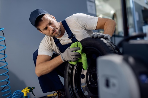 Reparador de automóveis limpando pneu de carro enquanto trabalhava em uma oficina