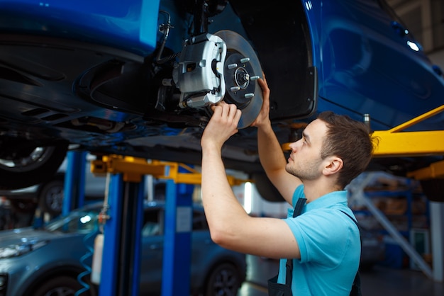 Reparador de uniforme, reparando veículo no elevador, estação de serviço do carro. verificação e inspeção de automóveis, diagnósticos profissionais e reparos