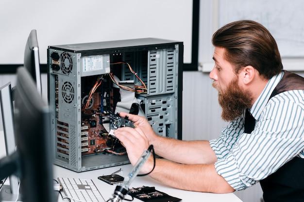 Reparador de desmontaje de la unidad de computadora para su reparación. Hombre barbudo sacando componentes electrónicos de la CPU. Renovación, arreglo, concepto de construcción