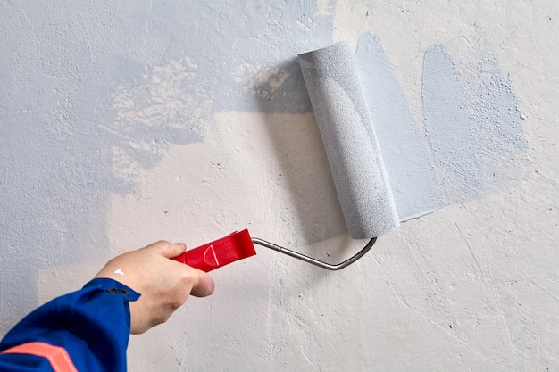 El reparador está pintando la pared con un rodillo de pintura durante la renovación.