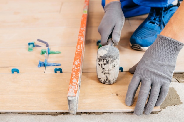 Reparador con guantes grises y baldosas uniformes con sistema de nivelación de baldosas en el suelo de la casa