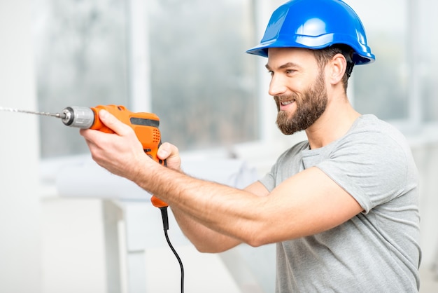 Reparador guapo en casco protector de perforación de la pared en el interior