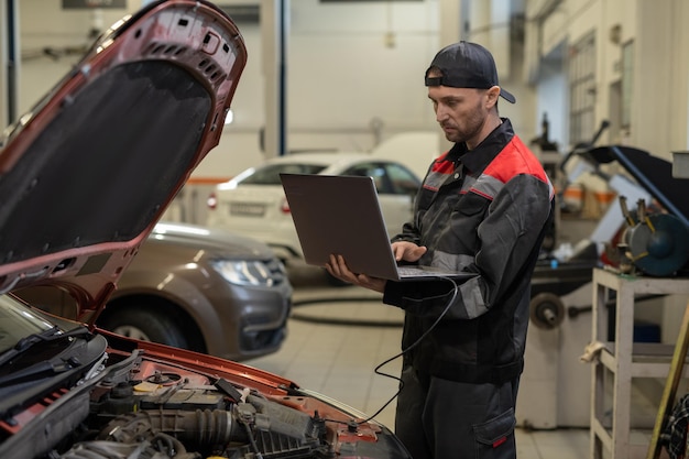 Reparador joven serio con computadora portátil que hace diagnósticos técnicos