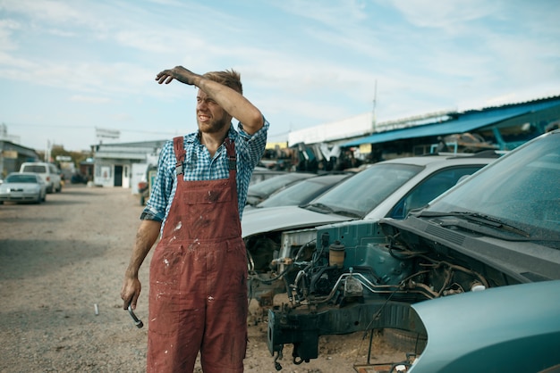 Reparador masculino cansado com a chave inglesa no ferro-velho do carro.