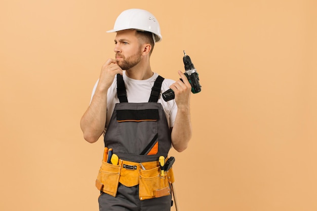 Reparador masculino positivo en casa sosteniendo un destornillador y pensando en un fondo beige