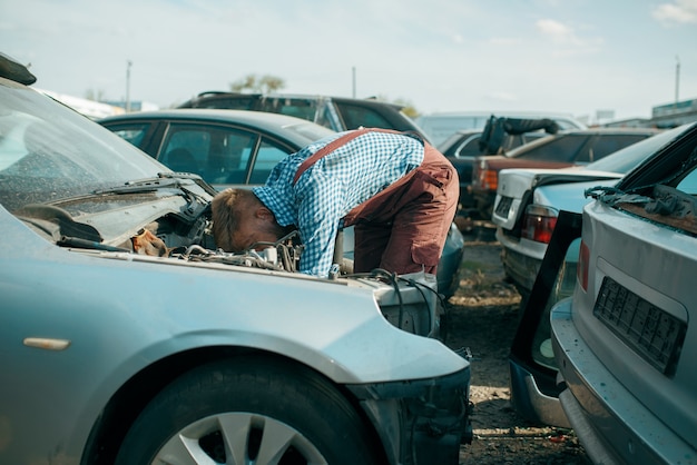 Reparador masculino trabaja en el depósito de chatarra de automóviles. chatarra de automóviles, chatarra de vehículos, basura de automóviles, transporte abandonado, dañado y aplastado