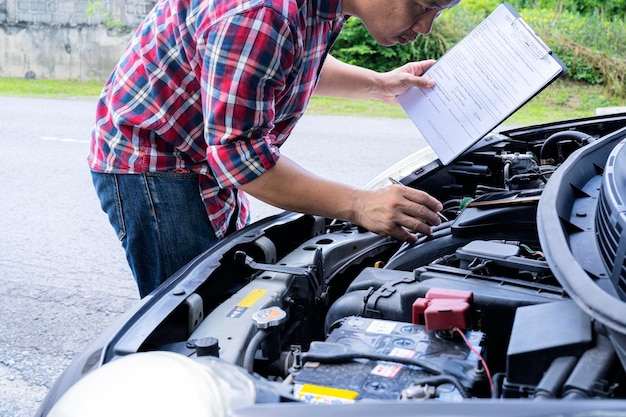 Foto reparador mecánico de automóviles revisando un motor de automóvil con inspección escribiendo en el portapapeles la lista de verificación