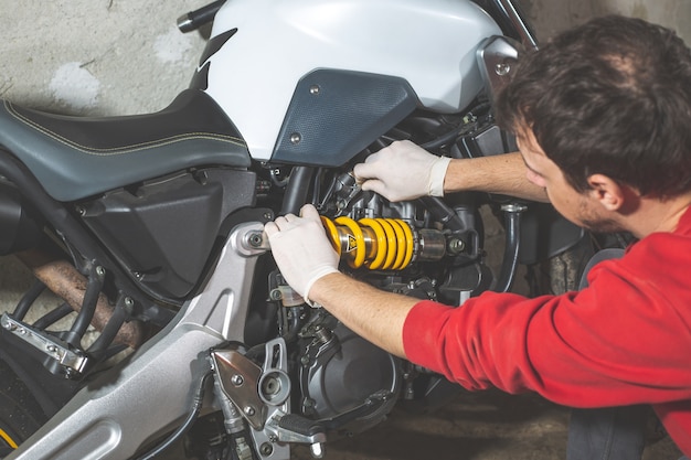 Reparador mecánico haciendo mantenimiento o reparación, fijación en la motocicleta, moto, centro de servicio