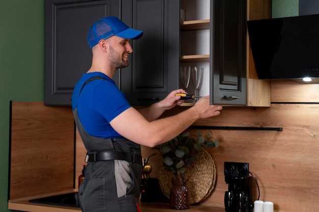 Foto reparador en mono reparando la bisagra del gabinete en la cocina mano masculina ajustando un mecanismo reparador