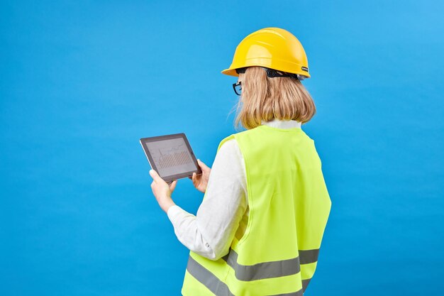 Foto reparador de mujer sosteniendo tableta ingeniero de niña sobre fondo azul de estudio reparador usa tableta mientras trabaja reparador de mujer mira hacia arriba en el gráfico jn tableta carrera de capataz