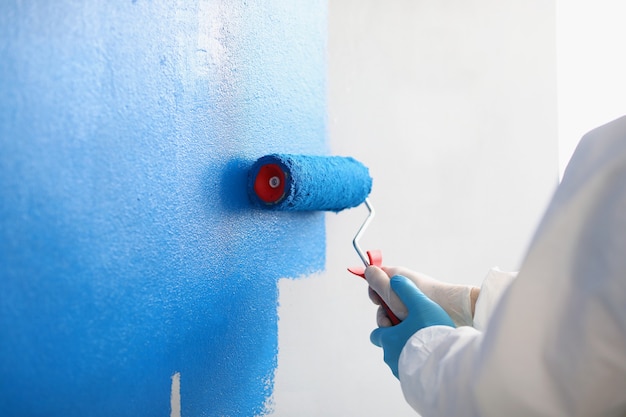 Reparador pintando la pared blanca en el apartamento azul con rodillo closeup