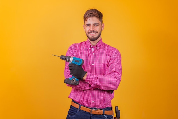 Foto reparador positivo y seguro con una camisa a cuadros y un kit de herramientas en la cadera y un destornillador eléctrico sonriendo y mirando a la cámara