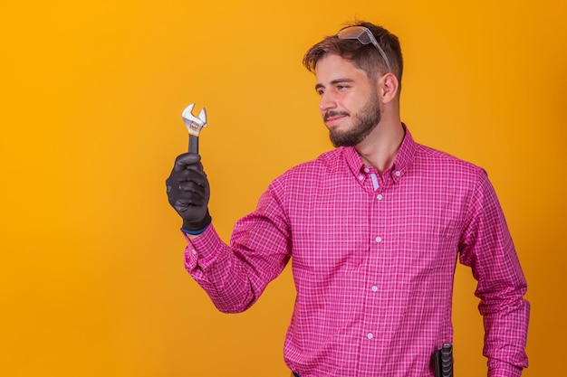 Reparador positivo y seguro con el kit de herramientas en la cadera y un destornillador sonriendo y mirando a la cámara, contra el fondo blanco.