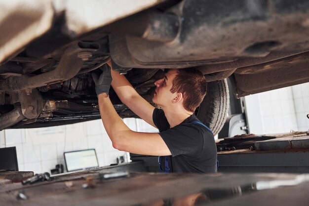 Reparador profesional en camisa negra trabaja bajo automóvil roto