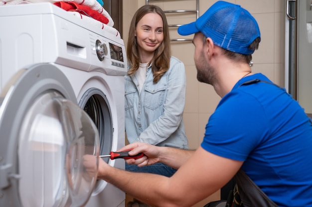 Reparador repara una lavadora delante de una mujer un hombre se comunica con el dueño de una lavadora