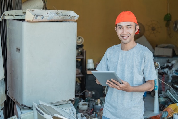 reparador sorri para a câmera enquanto usa seu tablet pc em torno de eletrônicos quebrados em uma oficina