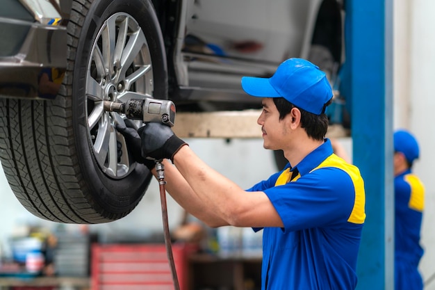 Reparador y técnico en el servicio de garaje con uniforme azul y sonrisa con herramientas en la mano.