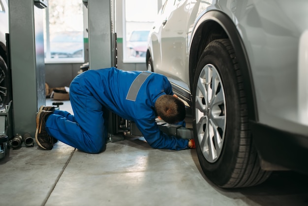 Reparador en uniforme ajusta el gato elevador en el servicio de automóviles, diagnóstico de suspensión. Servicio de automóvil, mantenimiento de vehículos