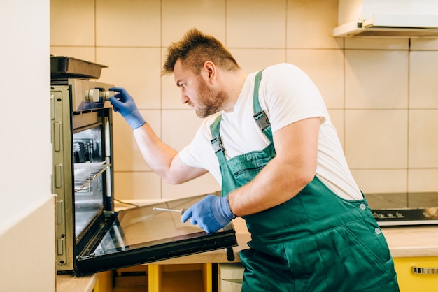 Reparador en uniforme comprueba el horno, técnico