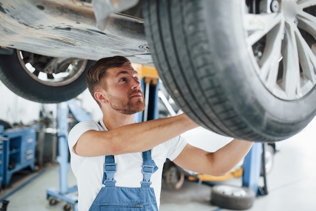 Reparando em ação. Funcionário com uniforme azul trabalha no salão automóvel