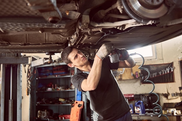 Foto reparar al hombre que arregla el automóvil en la estación de reparación debajo del automóvil levantado durante la reparación en el garaje