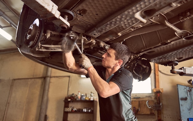 Reparar al hombre que arregla el automóvil en la estación de reparación debajo del automóvil levantado durante la reparación en el garaje