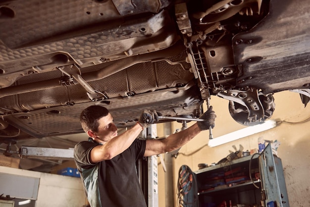 Reparar al hombre que arregla el automóvil en la estación de reparación debajo del automóvil levantado durante la reparación en el garaje