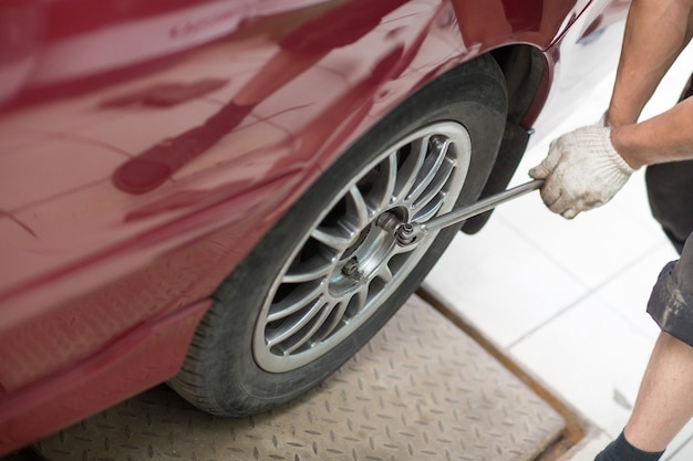 Reparar o cambiar el neumático del automóvil mecánico de vehículos atornillando la rueda del automóvil en la estación de servicio de reparación.