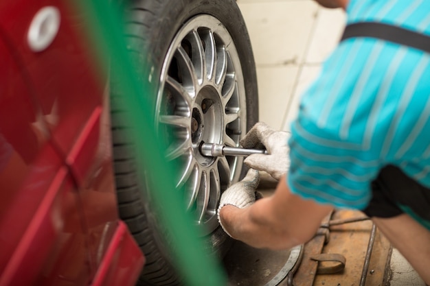Reparar o cambiar el neumático del automóvil mecánico de vehículos atornillando la rueda del automóvil en la estación de servicio de reparación.